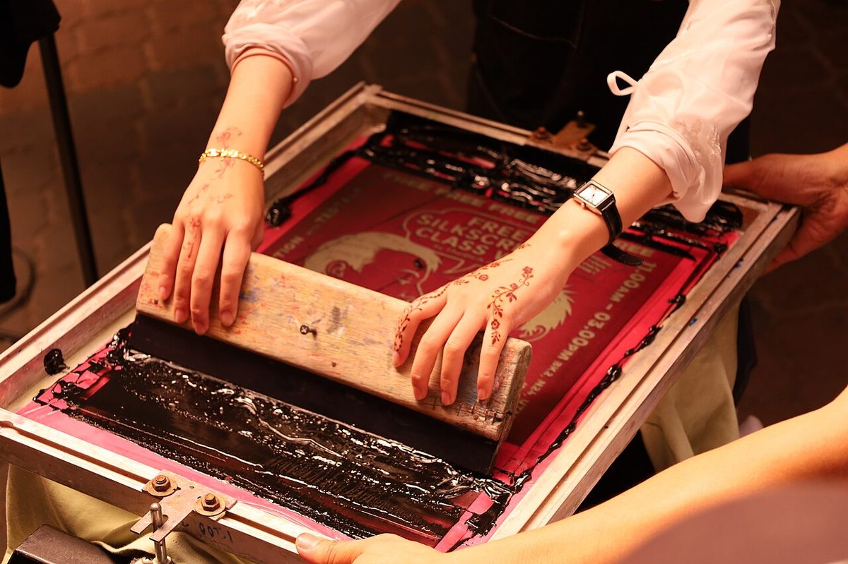 Manual screen printing: squeegee angle, pressure and stroke speed depend on the operator, and every sheet is placed and removed by hand.
